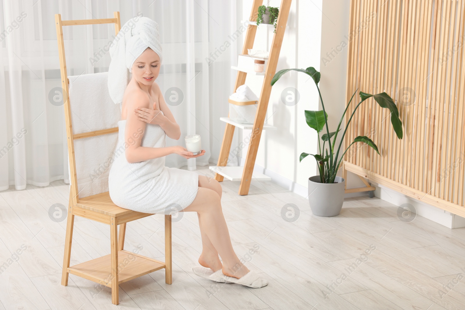 Photo of Beautiful young woman applying body cream onto shoulder indoors