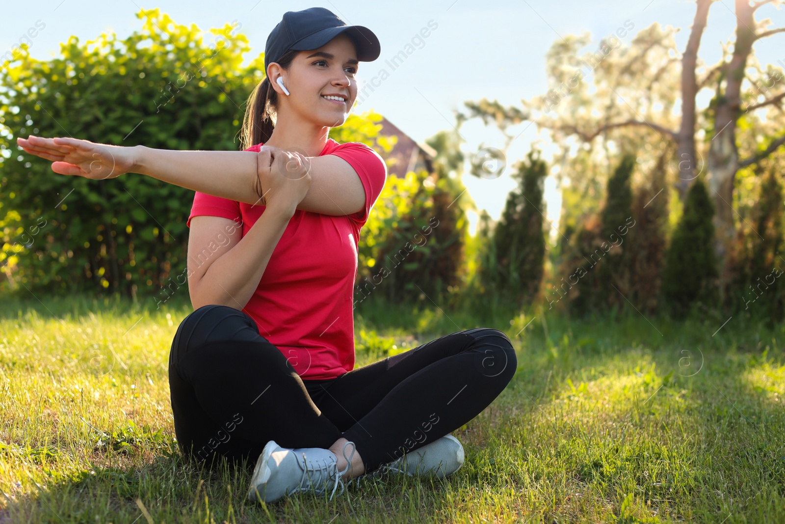 Photo of Young woman listening to music while doing morning exercise on green grass in park, space for text