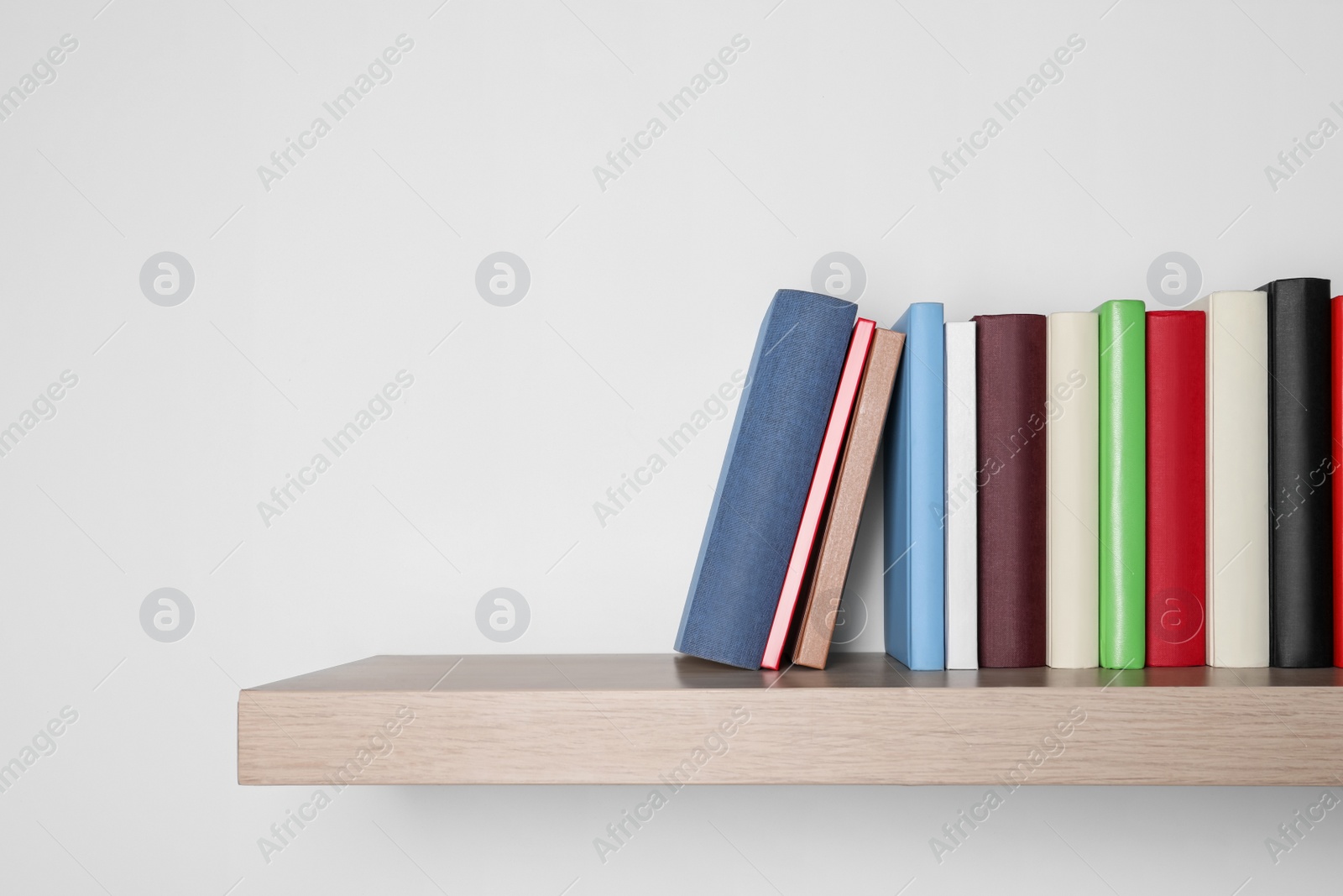 Photo of Different books on wooden shelf near white wall, space for text