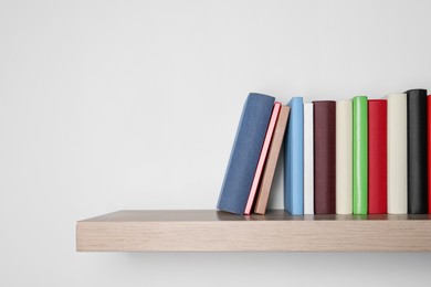 Different books on wooden shelf near white wall, space for text