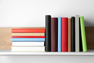 Photo of Many hardcover books on wooden shelf near white wall