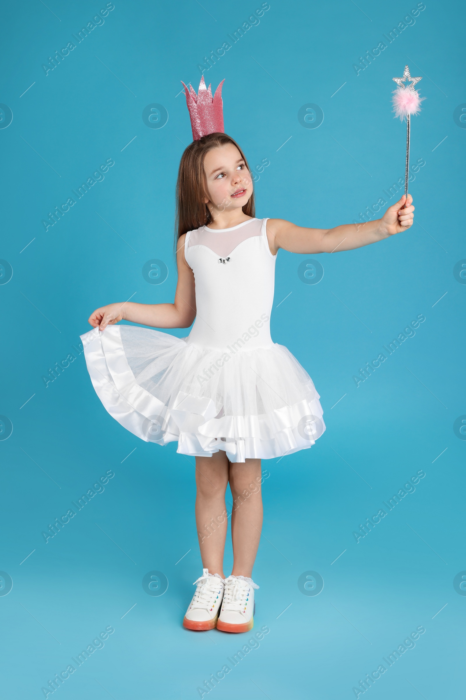 Photo of Cute girl in pink crown with magic wand on light blue background. Little princess