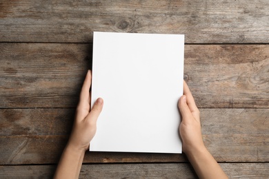 Photo of Woman holding brochure with blank cover on wooden background, top view. Mock up for design