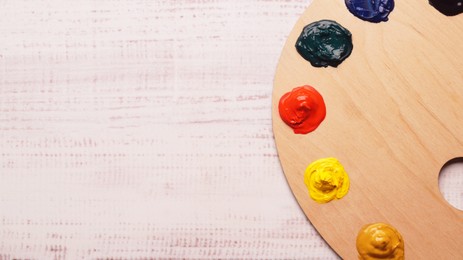 Artist's palette with samples of colorful paints on white wooden table, top view. Space for text