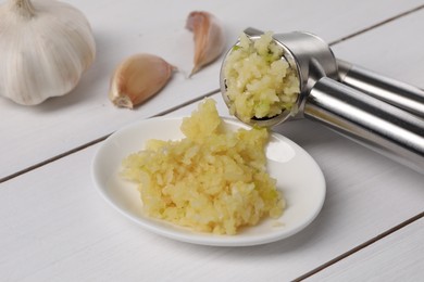 Photo of One metal press and garlic on white wooden table, closeup