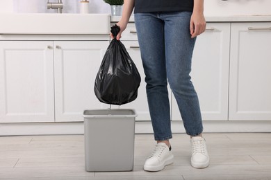 Photo of Woman taking garbage bag out of trash bin in kitchen, closeup