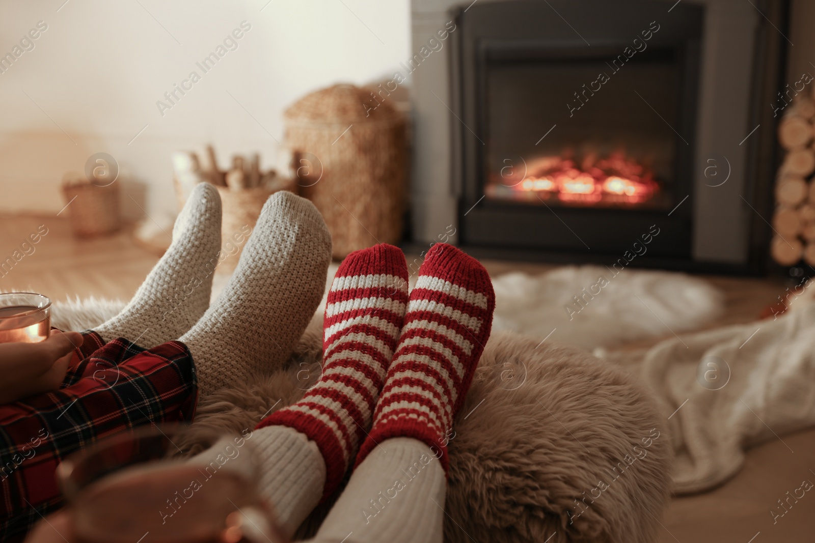 Photo of Couple in knitted socks near fireplace at home, closeup of legs