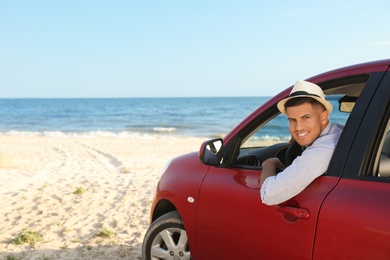 Photo of Happy man leaning out of car window on beach, space for text. Summer trip