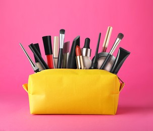 Image of Cosmetic bag filled with makeup products on pink background