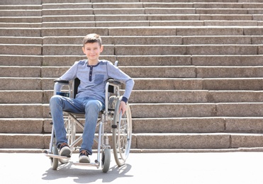 Preteen boy in wheelchair at stone stairs outdoors