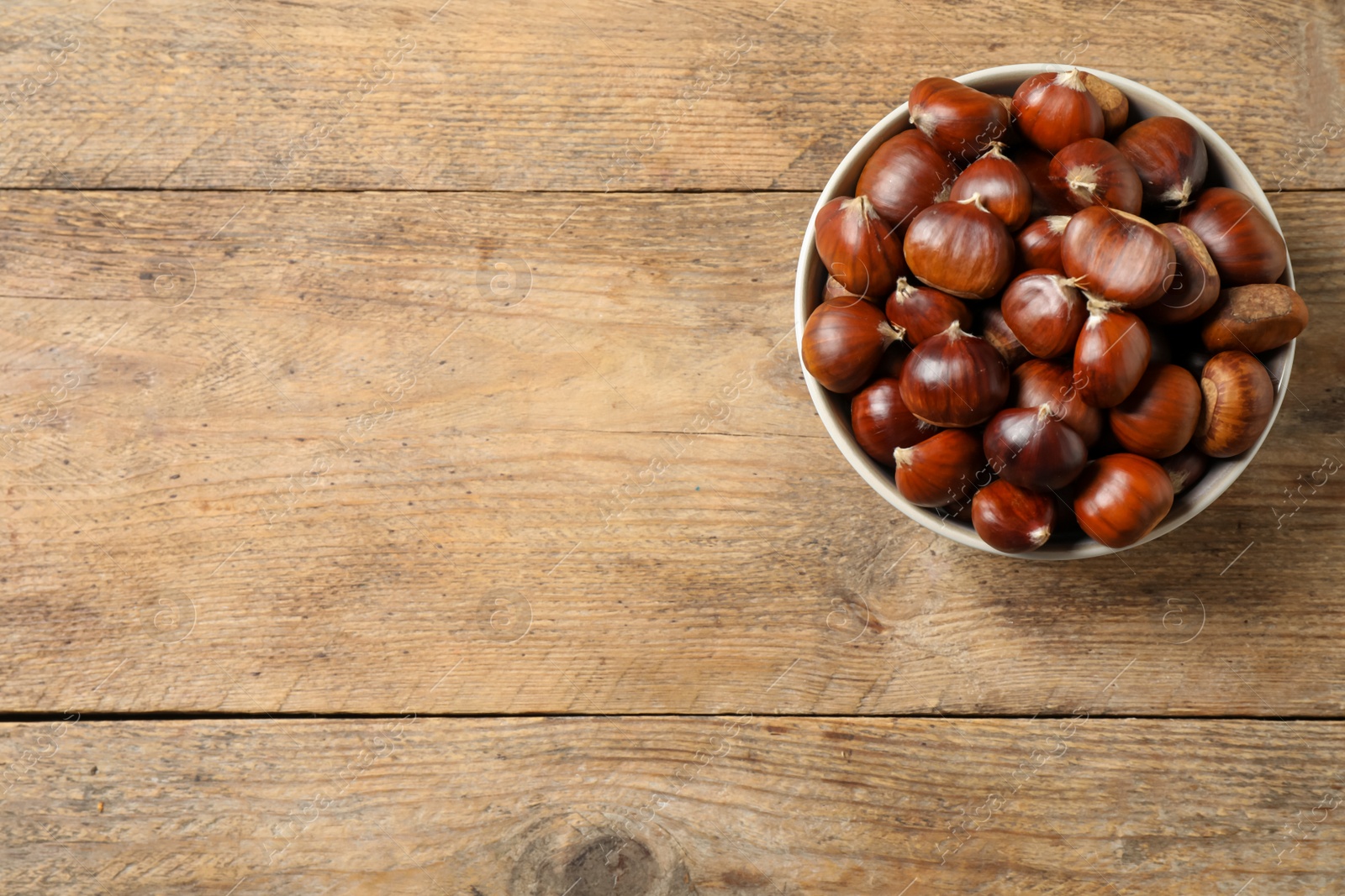 Photo of Fresh sweet edible chestnuts in bowl on wooden table, top view. Space for text