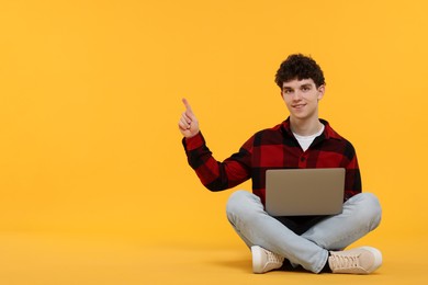 Portrait of student with laptop pointing on orange background. Space for text