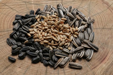 Photo of Pile of different sunflower seeds on wooden stump, closeup