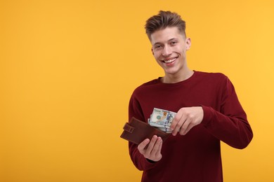 Photo of Happy man putting money into wallet on yellow background. Space for text