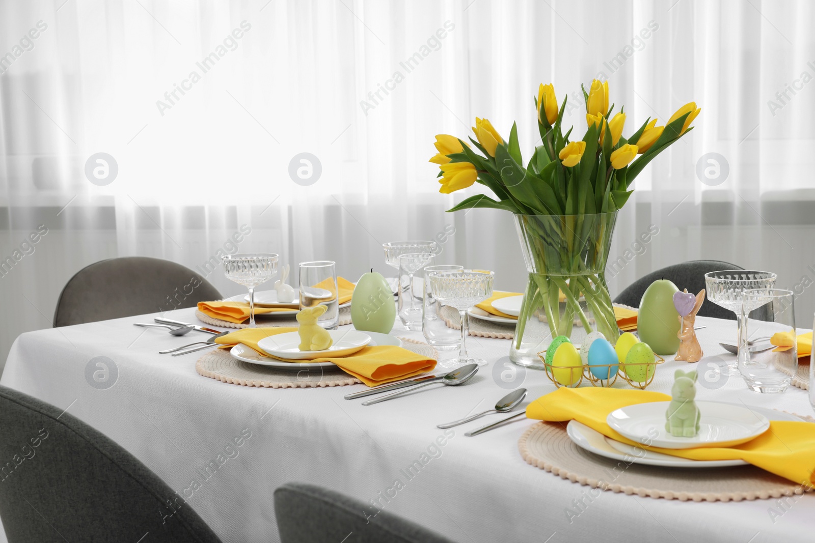 Photo of Festive table setting with glasses, painted eggs and vase of tulips. Easter celebration