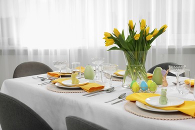 Photo of Festive table setting with glasses, painted eggs and vase of tulips. Easter celebration