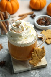 Photo of Cup of pumpkin spice latte with whipped cream, cookies and ingredients on light grey table, closeup