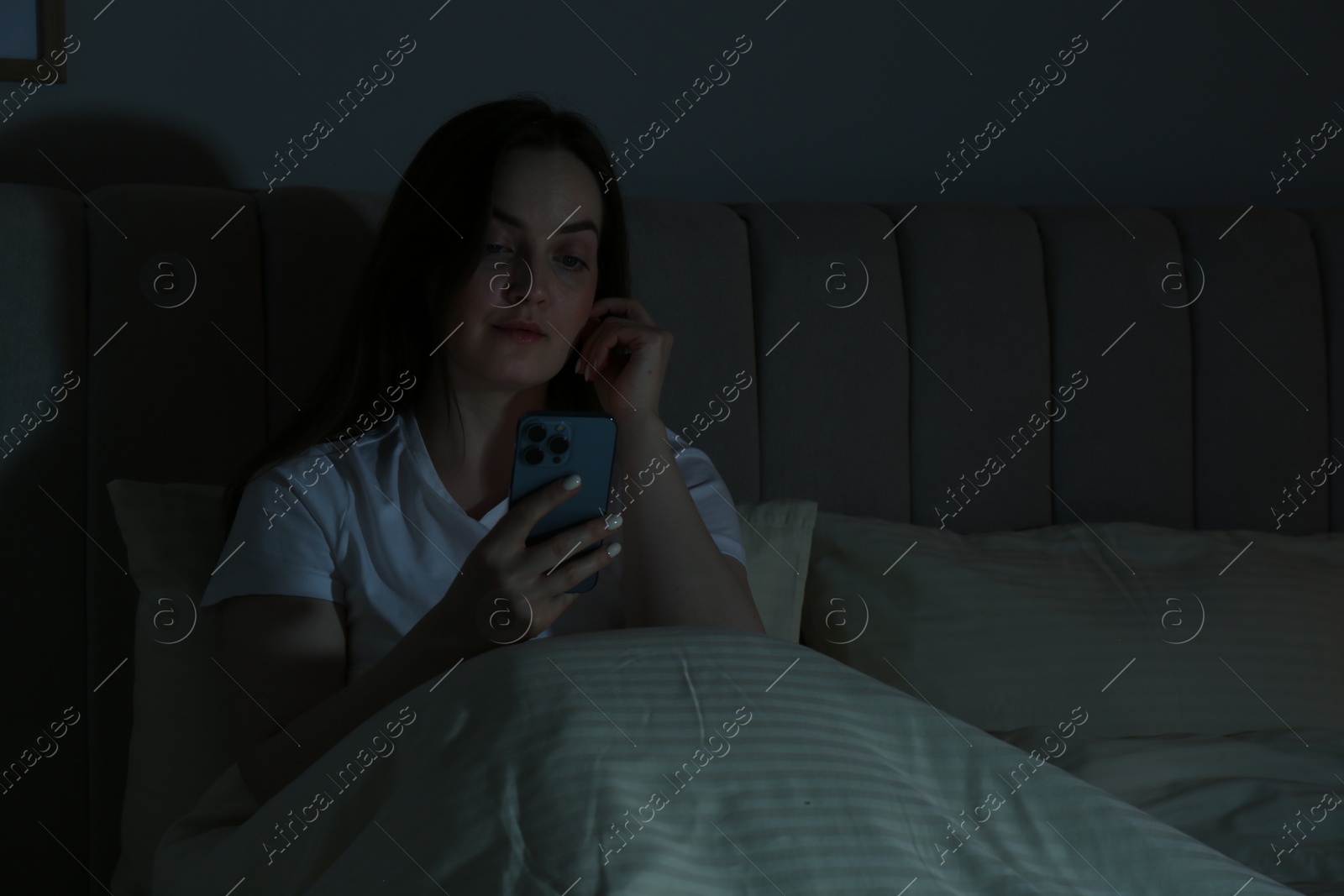 Photo of Woman using smartphone in bed at night. Internet addiction