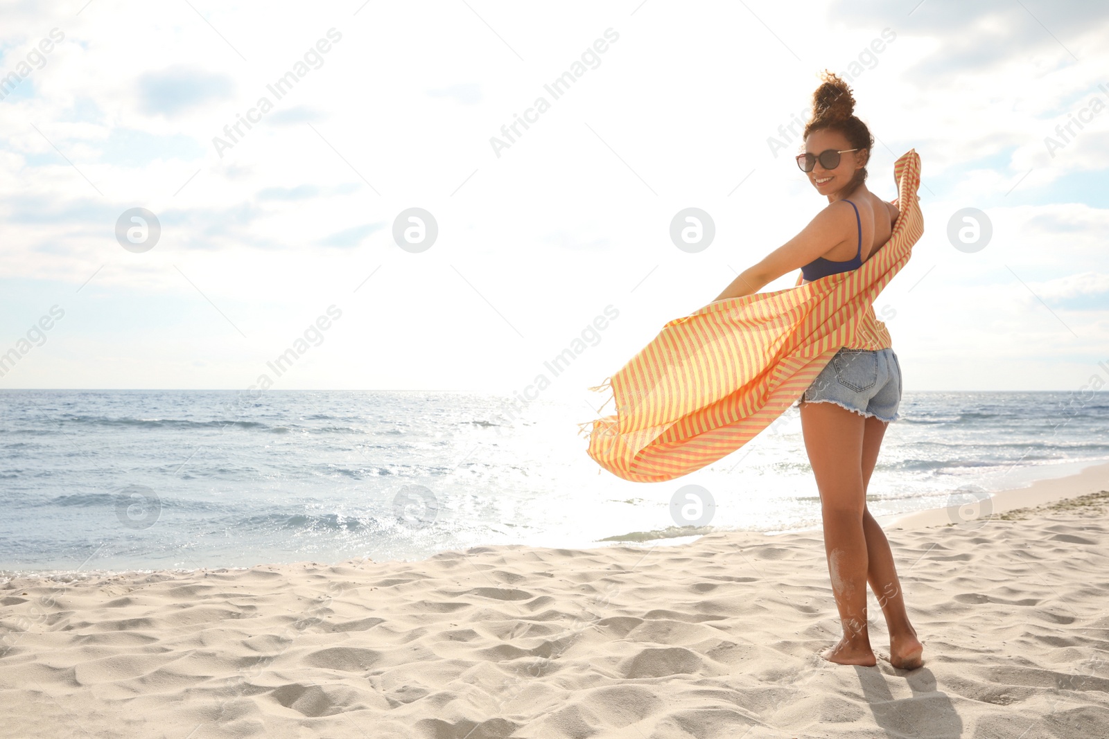 Photo of Beautiful African American woman with beach towel on sunlit seashore