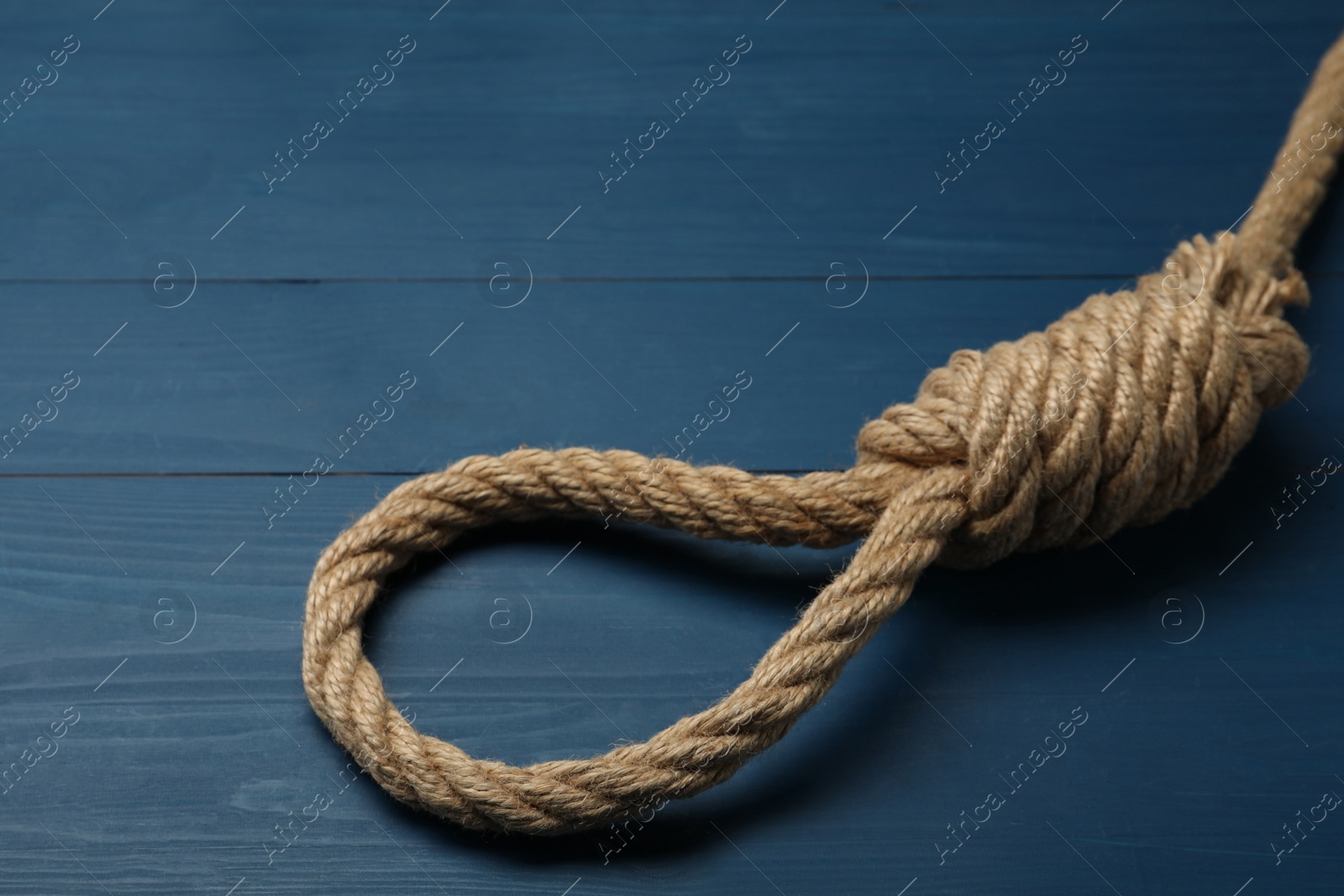 Photo of Rope noose with knot on blue wooden table, closeup