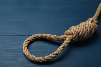 Rope noose with knot on blue wooden table, closeup