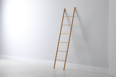 Photo of Modern wooden ladder near white wall indoors