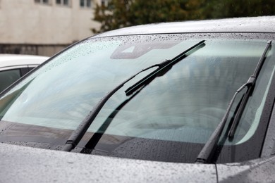 Photo of Car wipers cleaning water drops from windshield glass outdoors, closeup