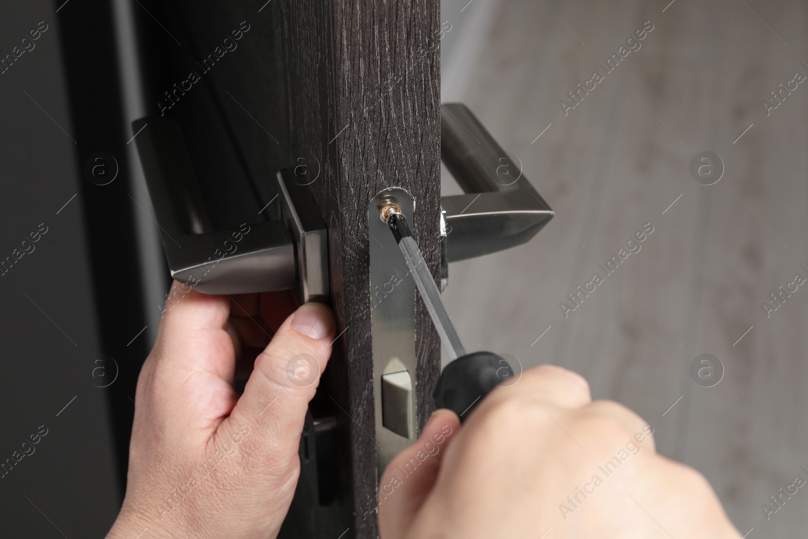 Photo of Handyman with screwdriver repairing door handle indoors, closeup