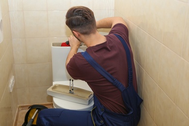 Photo of Male plumber repairing toilet tank in bathroom