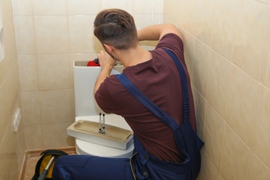 Male plumber repairing toilet tank in bathroom