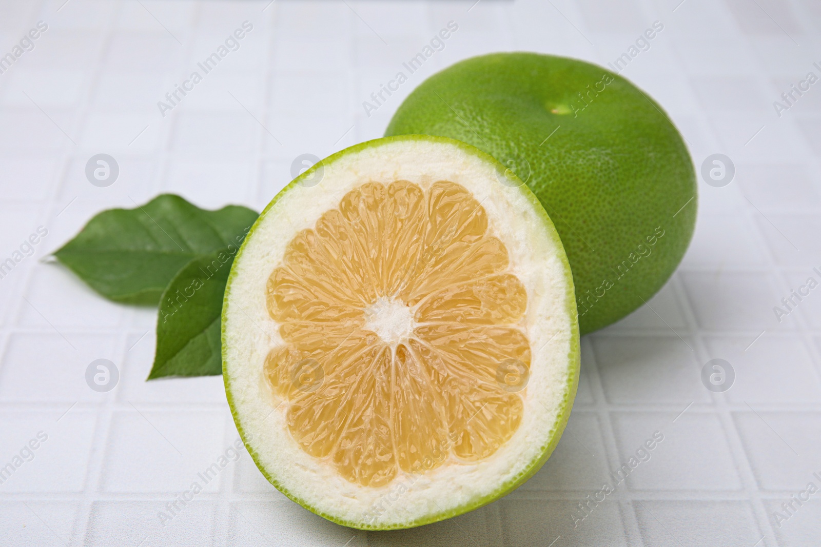 Photo of Whole and cut sweetie fruits with green leaves on white tiled table, closeup