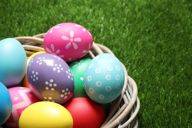 Photo of Colorful Easter eggs in decorative nest on green grass, closeup