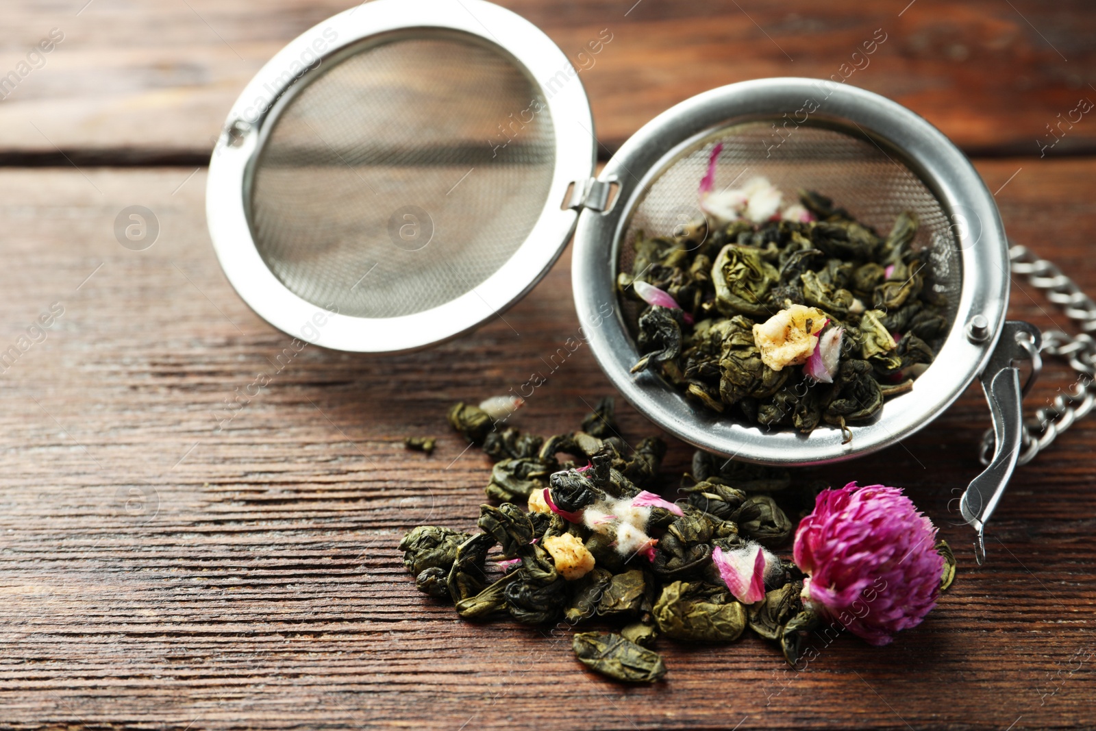 Photo of Snap infuser with dried herbal tea leaves and flowers on wooden table, closeup. Space for text