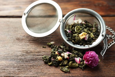 Photo of Snap infuser with dried herbal tea leaves and flowers on wooden table, closeup. Space for text