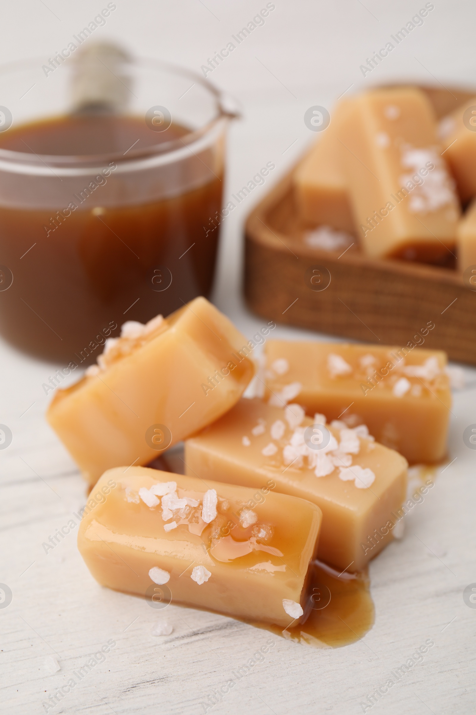 Photo of Yummy caramel candies, sauce and sea salt on white wooden table, closeup