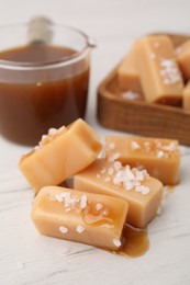 Yummy caramel candies, sauce and sea salt on white wooden table, closeup