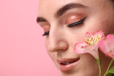 Photo of Beautiful woman with fake freckles and flowers on pink background, closeup. Space for text