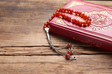 Photo of Muslim prayer beads and Quran on wooden table, closeup. Space for text