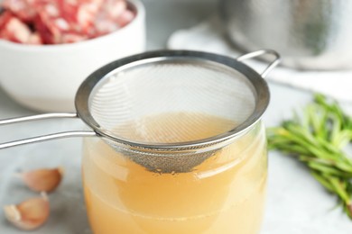 Photo of Glass jar with delicious bone broth and sieve on table, closeup