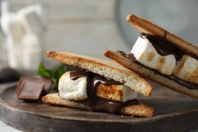 Photo of Delicious marshmallow sandwiches with chocolate on wooden tray, closeup