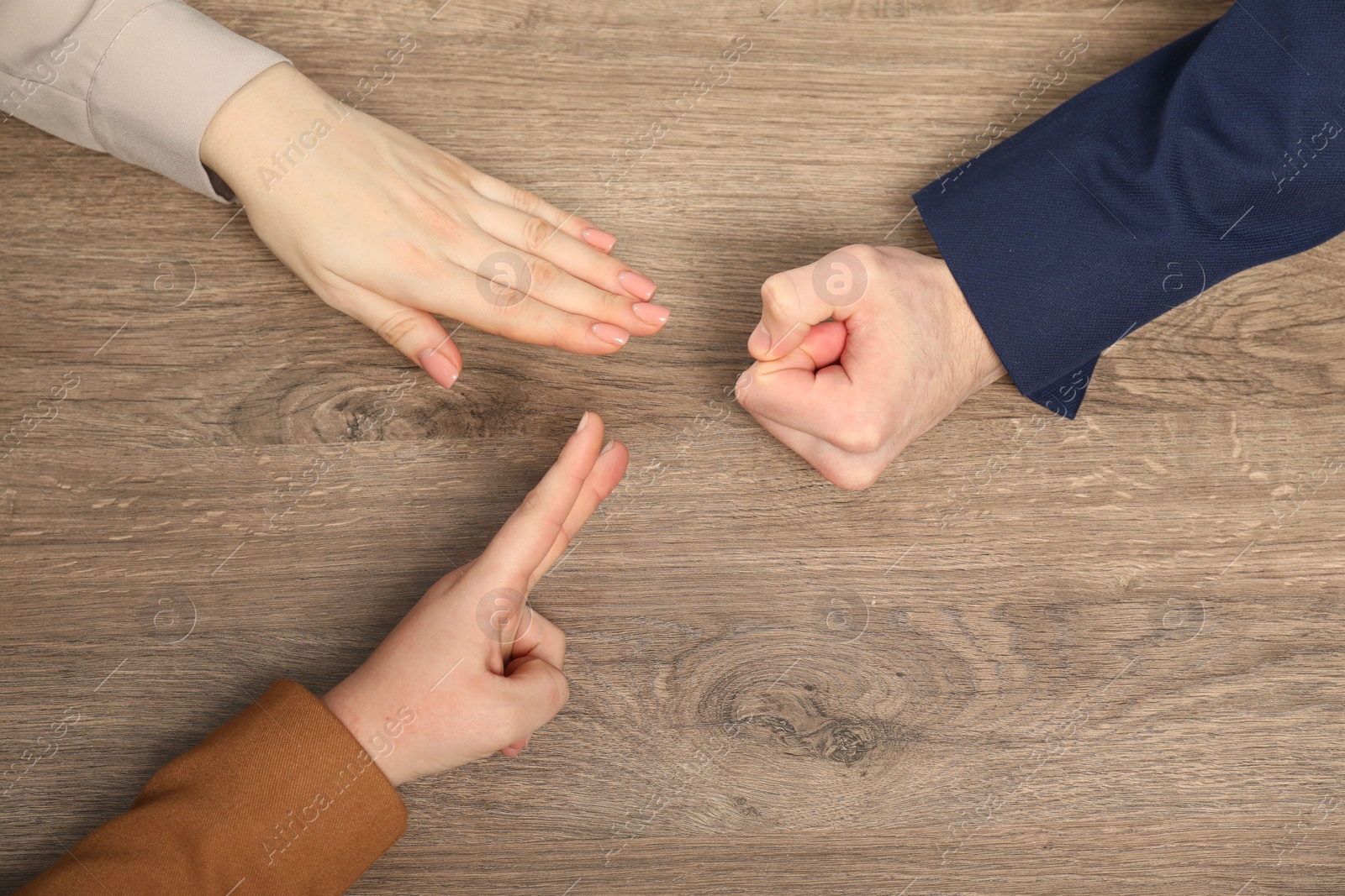 Photo of Closeup of people playing rock, paper and scissors on wooden background, top view