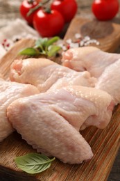 Photo of Raw chicken wings with basil on wooden board, closeup