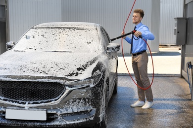 Photo of Businessman cleaning auto with high pressure water jet at self-service car wash
