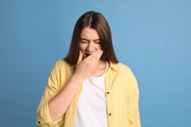 Photo of Young tired woman yawning on light blue background