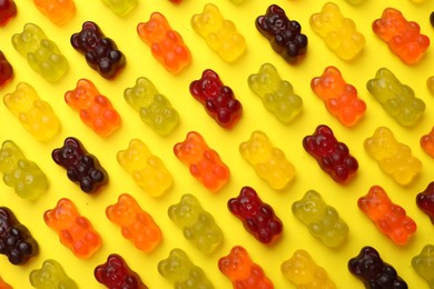 Photo of Delicious gummy bear candies on yellow background, flat lay