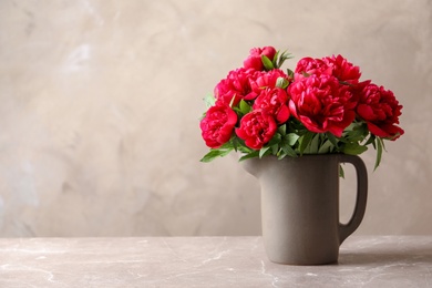 Photo of Pitcher with beautiful blooming peonies on table