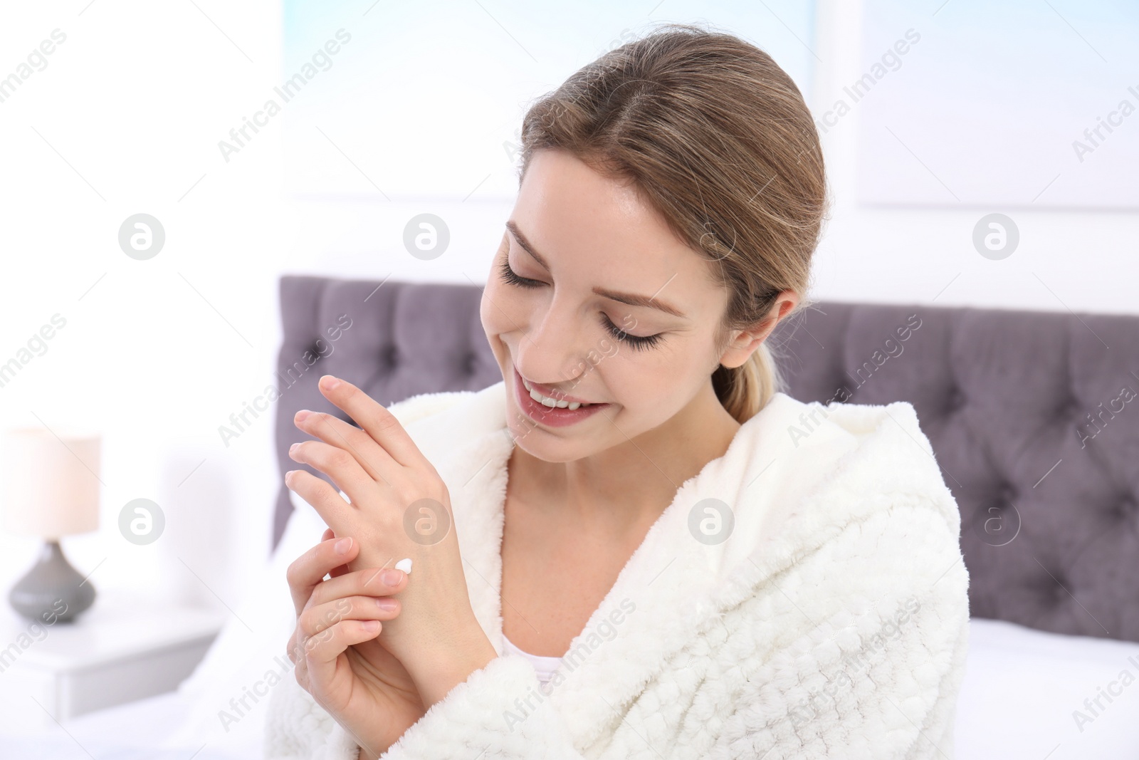 Photo of Young woman applying cream on her hands indoors. Beauty and body care