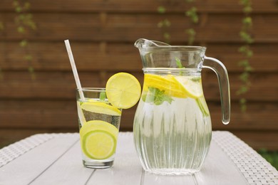 Photo of Water with lemons and limes on white wooden table outdoors