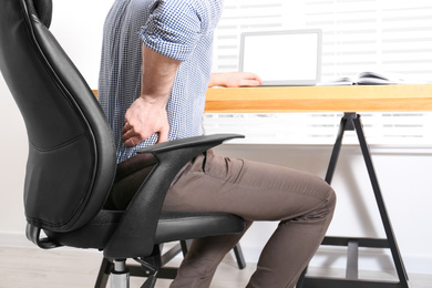 Photo of Man suffering from back pain at workplace in office, closeup