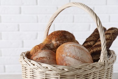 Photo of Different types of bread in wicker basket against white brick wall, closeup